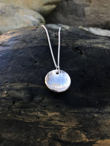 Linear Handmade Textured Sterling Silver Pendant On Rocks In Cornwall.