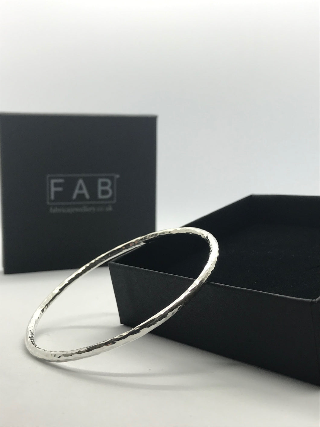 Solid silver hammered texture finish bangle sparkling in the light, resting on its jewellery box. Made from 3mm thickness Sterling silver wire.